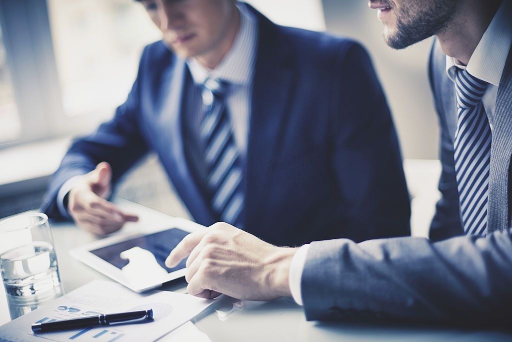 Image of two young businessmen using touchpad at meeting